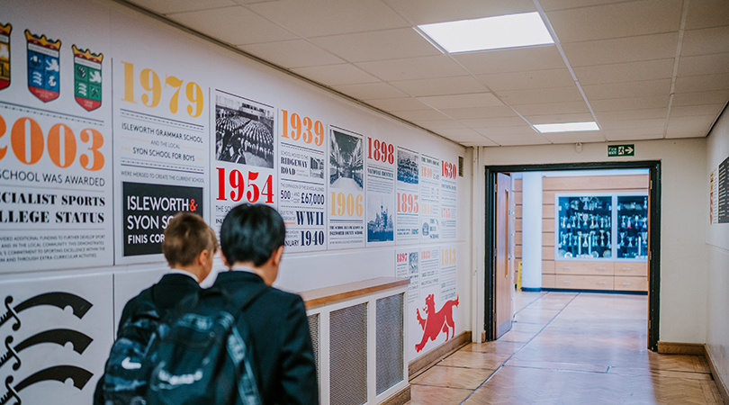 Students walk down a corridor. On the wall to the left is a visual timeline of the school's history.