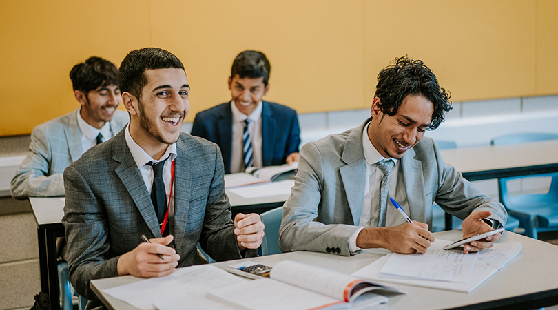 Two Sixth Form students, wearing suit, share a laugh during a maths lesson.