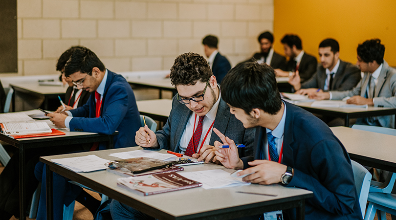 Two Sixth Form students, dressed in suits, discuss a maths problem in class.